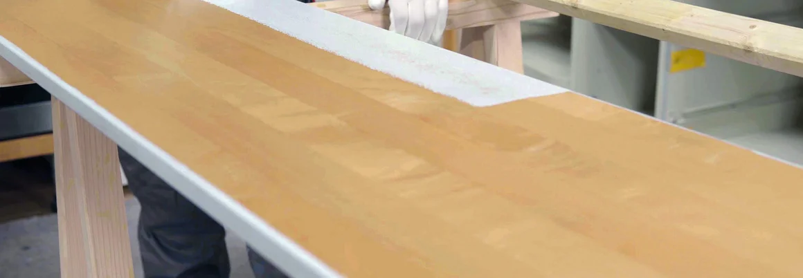 Person streicht Holzplatte mit Rolle weiß.